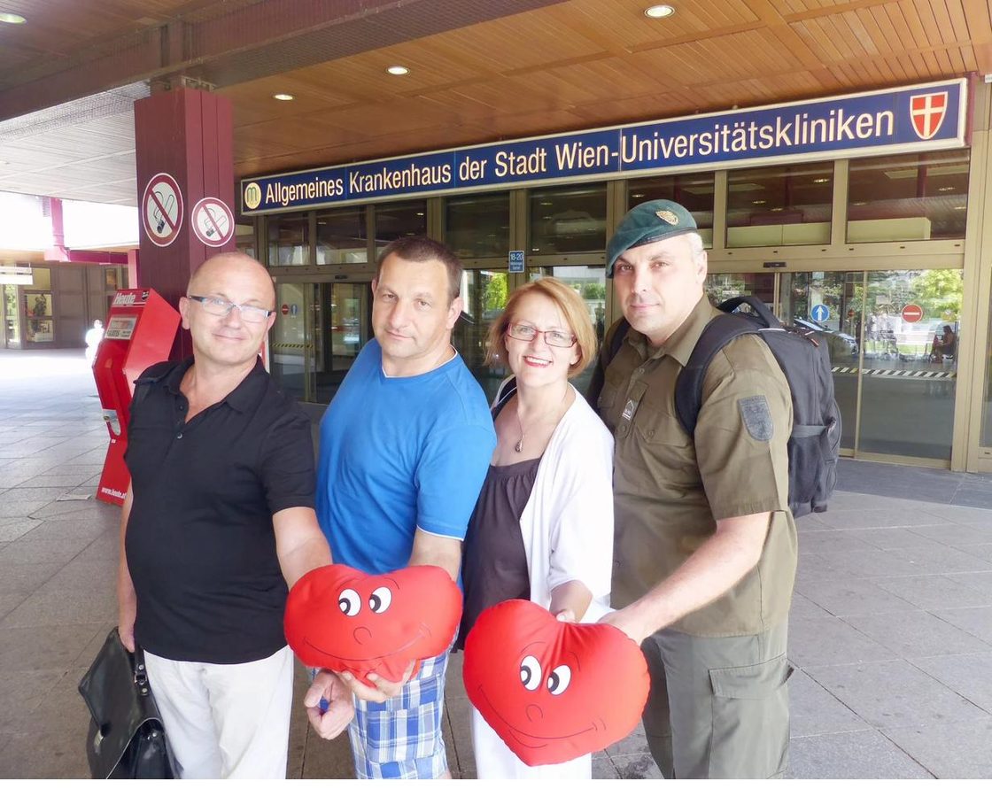 Project team in front of the entrance of Vienna General Hospital holding red heart cushions