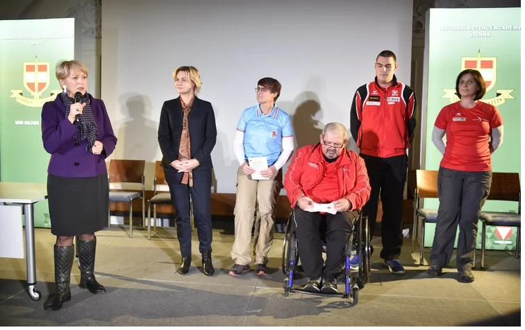 Podium mit sechs Personen, darunter ein Rollstuhlfahrer und Sportler:innen in Trainingsanzügen